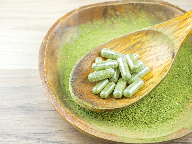 Kratom capsules in a wooden spoon