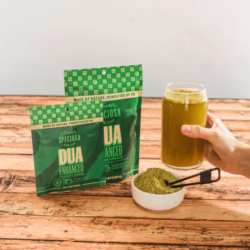 dua enhanced kratom bags on table, next to hand holding a glass of kratom drink